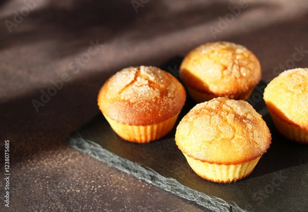 Fototapeta Dessert muffins with sugar crust on a black stand on a dark background