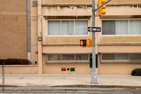 Fototapeta Semáforo para peatones en una calle de Nueva York, USA. Semáforo con una mano en rojo indicando prohibido cruzar a peatones. Junto al semáforo una señal con flecha de sentido obligatorio.