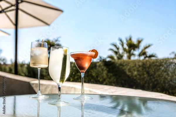 Fototapeta A variety of cocktails in different types of glasses on a glass-topped table. Midday happy hour time in tropical climate. Resort, holiday refreshment concept.