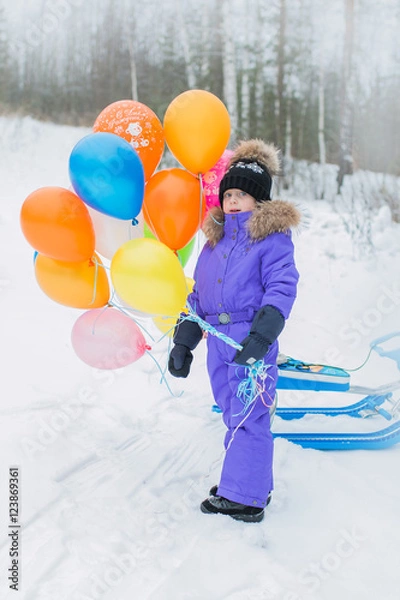 Fototapeta Cheerful girl walks in the winter in the forest on the mountain. she holds in her hand a lot of multi-colored balloons.