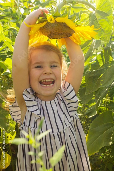 Obraz Little beautiful smiling girl holding sunflower flower in sunflower field in summer