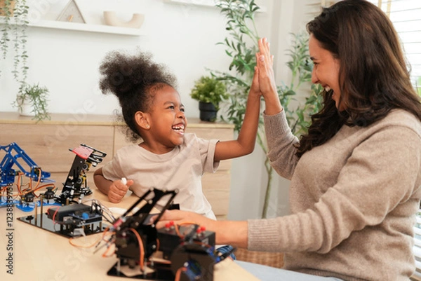 Obraz Excited mother and daughter giving a high five after successfully assembling a robotics project, enjoying a fun and educational STEM activity that fosters teamwork and creativity at home