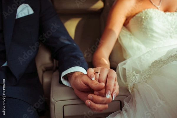 Fototapeta Closeup of newlyweds hands held together on the seat of a car