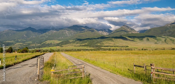Fototapeta Low lying clouds cover the beautiful mountain range in Wyoming with a dirt road leading off into the distance in a Panoramic Image