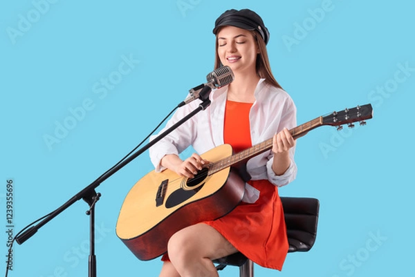 Obraz Young woman with microphone and guitar singing on blue background