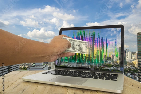 Obraz Fintech for investment concept image. Hand pull money out of computer screen with binary code againt City background. Representing fintech involved in investment business.