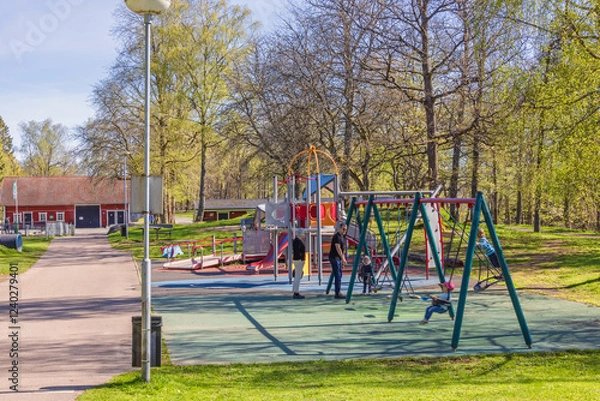 Fototapeta Playing children at a playground with a swing set at spring