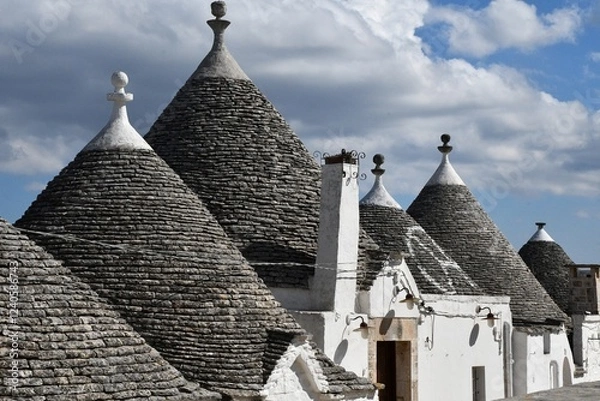 Fototapeta The grey stone and conical roofs of the trulli houses in Alberobello, with white stone wash walls. The sky is overcast with grey clouds.