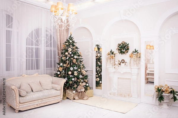 Fototapeta classic appartments with a white fireplace, decorated Christmas tree, bnight sofa, large windows and a chandelier in Baroque style