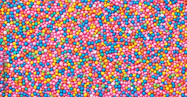 Fototapeta A  of colorful sprinkles on a pink background, viewed from above. The pastel and vibrant colors of the candy sprinkles create a playful and fun atmosphere, with space for text to personalize t