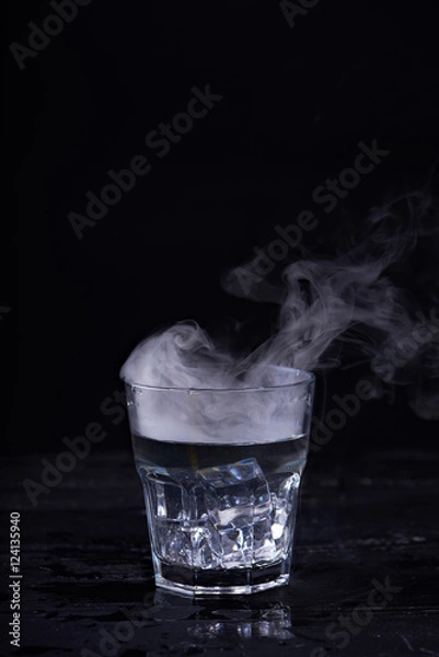 Fototapeta Hot water with a lot of steam in a glass at a black background. Dark photo. Concept photo: three state of water - ice, water, steam.