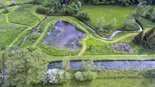 Obraz Aerial view of green lush fields surrounded by ponds, streams, trees, shrubs, walking paths in summer English countryside