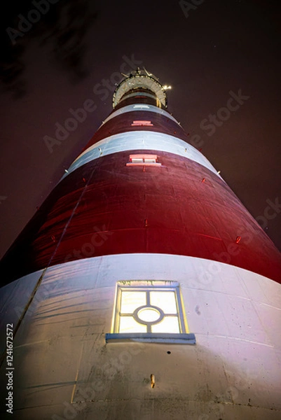 Fototapeta Majestic high up view of red with white striped lighthouse on Dutch Wadden Island at night time with stormy weather