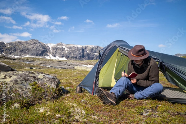 Fototapeta Hiking maie sitting in his tent opening writing in a notebook
