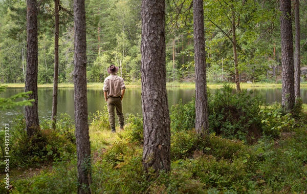 Fototapeta Man looking over a small lake in a forest