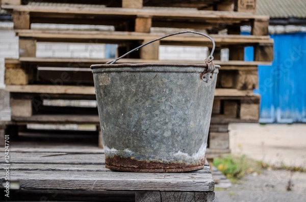 Fototapeta an old iron bucket in the garden at wooden pallet / an old rusty bucket / Old galvanised bucket /