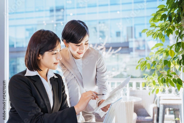 Obraz ビジネス街にある明るいオフィスで協力して仕事を進めるチームワークの良い2人の女性