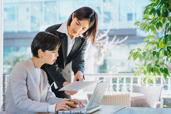 Obraz ビジネス街にある明るいオフィスの窓際でパソコンを前に真剣に仕事をする30代の2人の女性