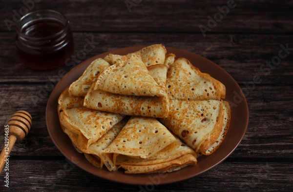 Fototapeta Baking openwork pancakes in a hole triangles on a plate on a dark background with honey
