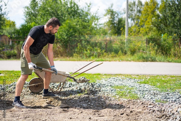 Fototapeta A man with a shovel loads crushed stone into a wheelbarrow