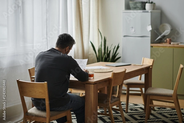 Fototapeta Contemplative afternoon with a handsome man immersed in reading at a cozy dining table