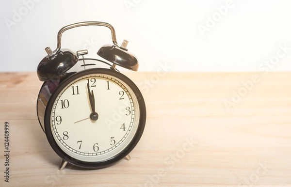 Fototapeta Alarm clock on a wooden plate with a white background.
