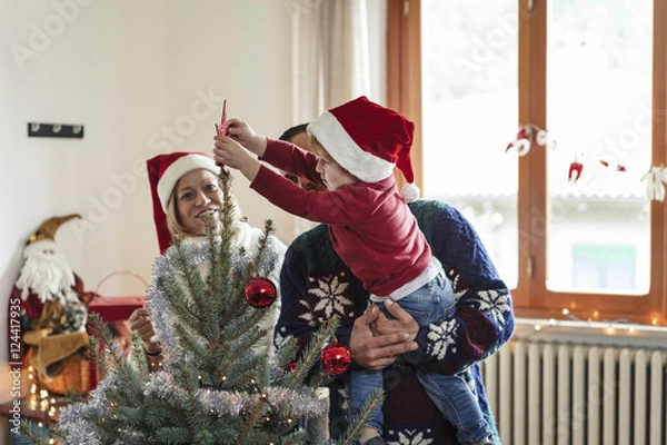 Obraz happy family with a young child decorating a christmas tree at h