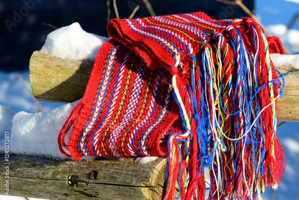 Fototapeta ceinture fléchée (traditional pattern) replica of the woven sash worn by voyageurs during the fur trade draped on wooden fence rail with snow at base in sunlight close up