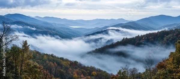 Fototapeta Misty mountain landscape with soft blue and gray valleys enveloped in clouds featuring vibrant green and golden foliage at the foreground