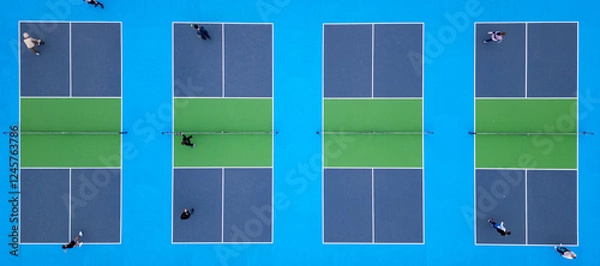 Fototapeta Aerial top-down view of multiple pickleball courts with players engaged in a match. The vibrant blue and green surfaces create a striking geometric pattern, capturing the dynamic movement and energy