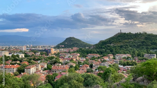 Fototapeta Scenic view of Plovdiv, Bulgaria, featuring the Alyosha monument, cityscape, lush hills, and cloudy sky. Take at Golden Hour.