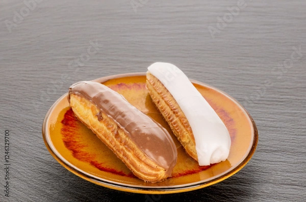 Fototapeta Two eclairs with cream filling on a ceramic saucer on a slate stone.