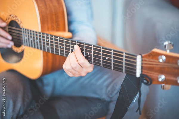 Fototapeta Close-up on musician strums an acoustic guitar in a cozy home, immersed in music. His casual style, warm lighting, and relaxed atmosphere create a serene, artistic, and inspiring moment