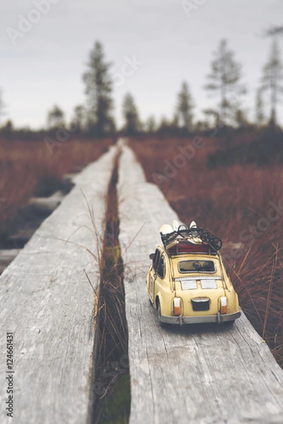 Fototapeta Miniature car is traveling around the world. Caricature car is wondering on a swamp. Duckboards going far away. Image has a vintage effect applied.