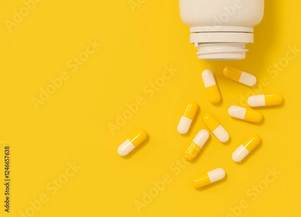 Fototapeta Yellow and white capsules spilled from white plastic bottle on yellow background. Top view with space for text.