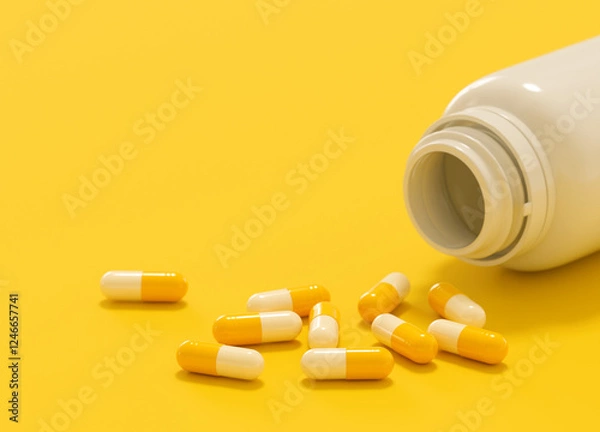 Fototapeta Some yellow and white capsules poured out of a plastic bottle on yellow background with copy space.
