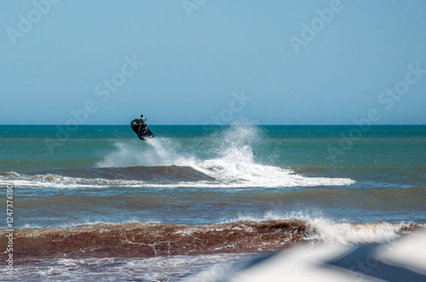 Fototapeta A jet ski jumping over the waves of the sea on a sunny day	