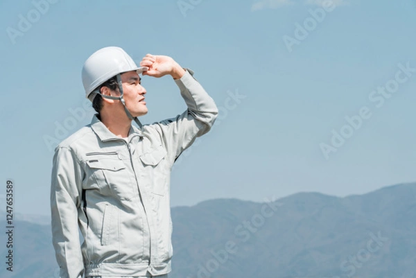 Fototapeta 青空の下に立つヘルメットを被った作業着姿の男性（建築・土木・建設）
