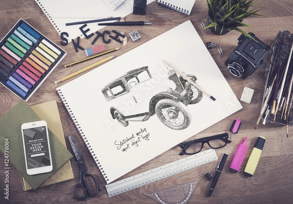 Fototapeta Sketchbook and Smartphone with Assorted Art Supplies on Wooden Desk Mockup 1