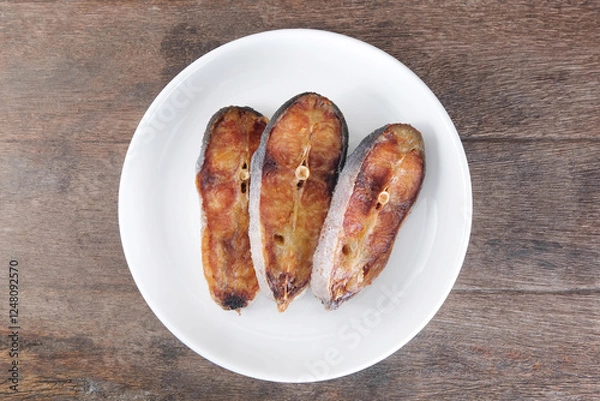 Obraz Sun-dried pangasius in a white ceramic plate on a wooden table.