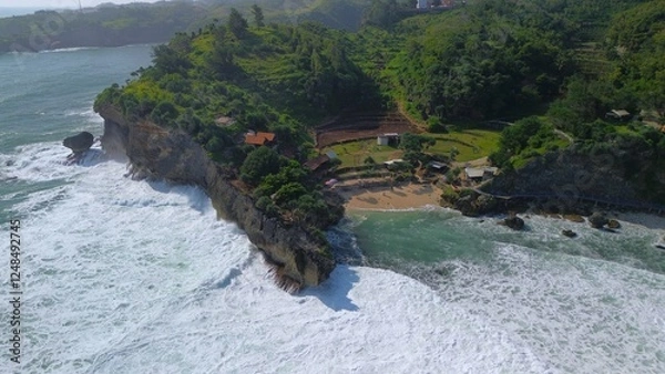Fototapeta Aerial Drone view of the beach with white sand, coral rocks, hills with trees, waves from the ocean which is a tourist destination known as Mbuluk Beach Gunung Kidul Yogyakarta