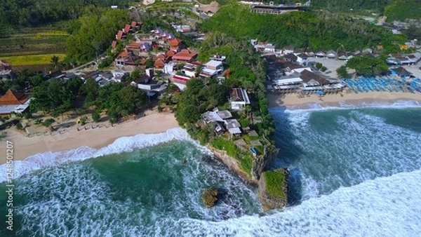 Fototapeta Aerial Drone view of the beach with white sand, coral rocks, hills with trees, waves from the ocean which is a tourist destination known as Drini Beach Gunung Kidul Yogyakarta