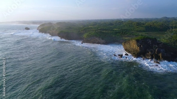 Fototapeta Aerial Drone view of the beach with white sand, coral rocks, hills with trees, waves from the ocean which is a tourist destination known as Krakal Beach Gunung Kidul Yogyakarta