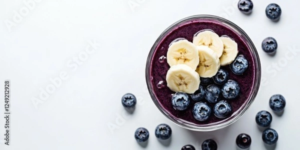 Fototapeta A playful glass of blueberry and banana smoothie topped with sliced bananas, set on a white background
