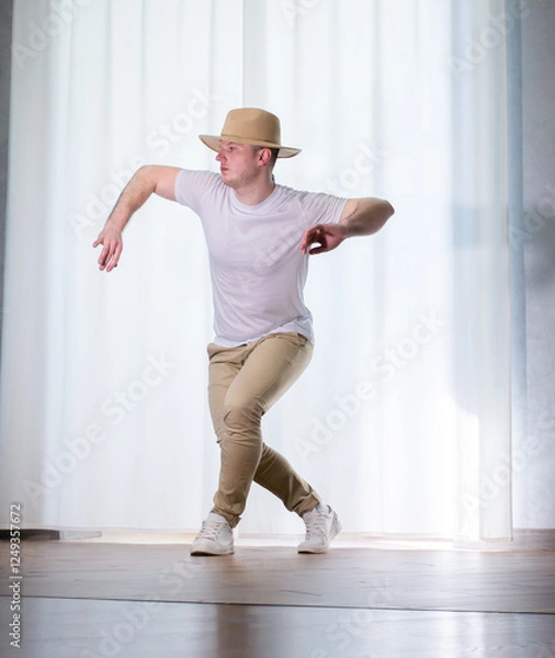Fototapeta Young guy dancer in motion in a pose. A man performs a modern dance in casual clothes.
