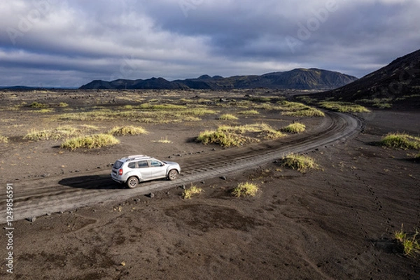 Obraz Aerial perspective of a car navigating a sparse basalt road Landmannalaugar in Iceland, surrounded by barren landscapes and bathed in warm sunlight
