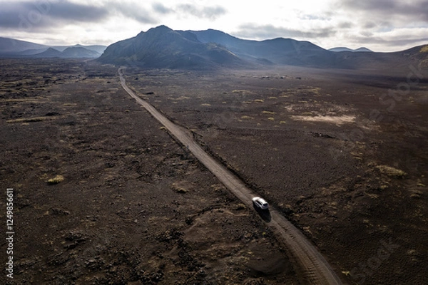 Obraz Aerial perspective of a car navigating a sparse basalt road Landmannalaugar in Iceland, surrounded by barren landscapes and bathed in warm sunlight