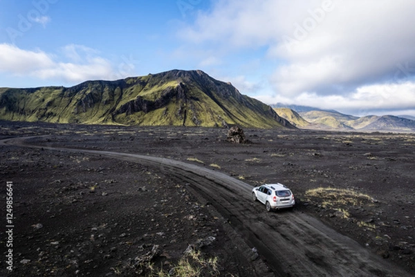 Obraz Aerial perspective of a car navigating a sparse basalt road Landmannalaugar in Iceland, surrounded by barren landscapes and bathed in warm sunlight