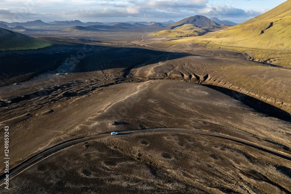 Obraz Aerial perspective of a car navigating a sparse basalt road Landmannalaugar in Iceland, surrounded by barren landscapes and bathed in warm sunlight