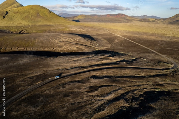 Obraz Aerial perspective of a car navigating a sparse basalt road Landmannalaugar in Iceland, surrounded by barren landscapes and bathed in warm sunlight